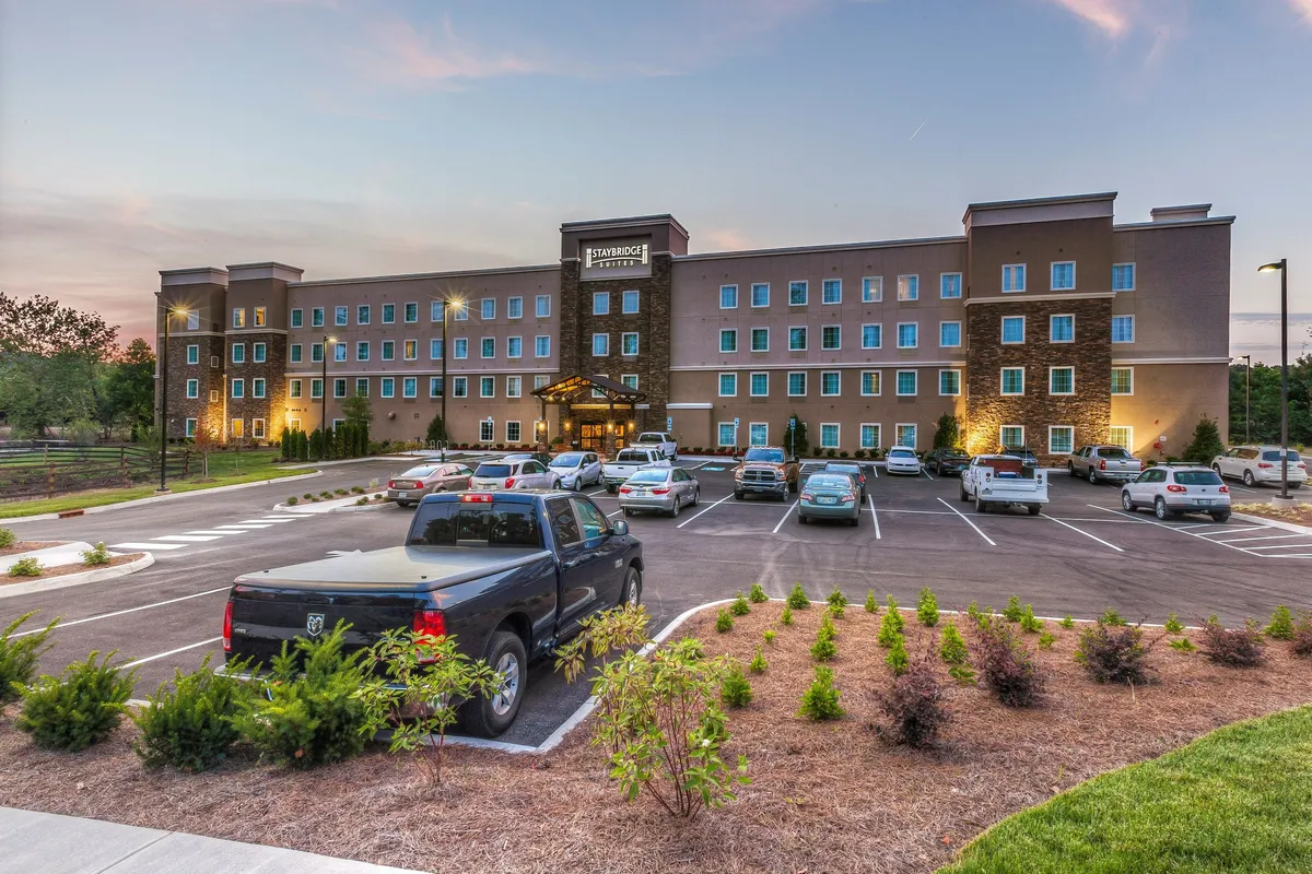 This image captures the hotel’s exterior entrance, with a well-maintained parking lot, attractive landscaping, and the inviting facade of the building. The scene is set during a warm sunset, creating a welcoming atmosphere for guests arriving or heading out for adventures.