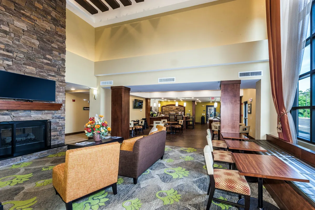 A welcoming living area highlighted by a stone fireplace, comfortable seating options, a colorful floral arrangement, and large windows that flood the space with natural light. The room invites relaxation and casual gatherings, reflecting an atmosphere where guests can unwind or enjoy entertainment.