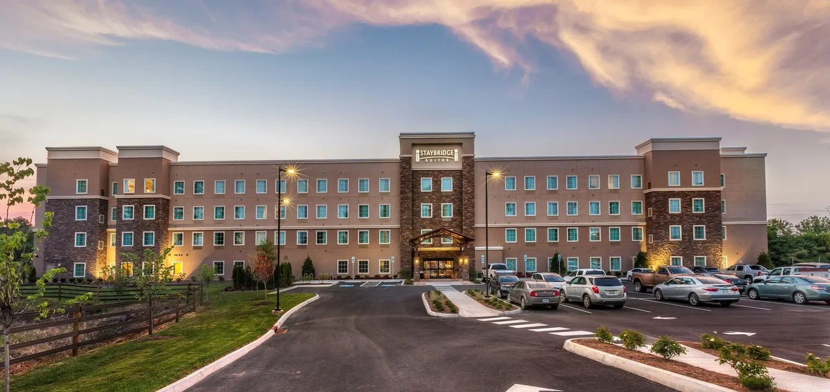 This image displays the hotel's exterior with a prominent entrance awning, landscaped areas, and a visible parking lot. The inviting facade suggests easy access for guests and an accessible transition point between the hotel and the surrounding attractions.