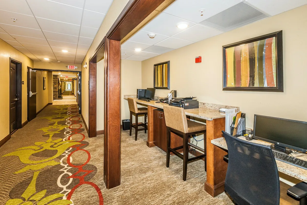 This image presents a welcoming business center with multiple computer workstations, colorful wall art, and a decorative carpet. The space is both productive and inviting, suitable for working, studying, or informal networking with other guests. The layout suggests a comfortable environment for guests who need to balance business with their stay.