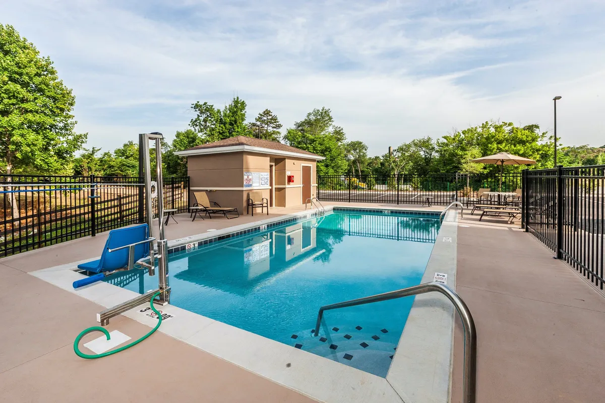 This image showcases the outdoor swimming pool surrounded by comfortable lounge chairs and a poolside gazebo. The setting is inviting, with the pool glistening under natural light and relaxed guests seen swimming, sunbathing, and conversing in small groups. The pool area appears well-maintained and is ideal for both quiet relaxation and social gatherings, reflecting the amenity's dual purpose for leisure and mingling.
